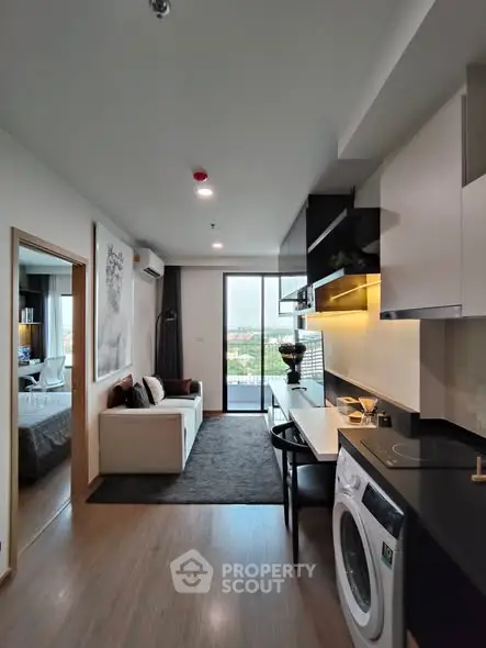 Modern open-plan living room with kitchen and washing machine, featuring sleek design and natural light.