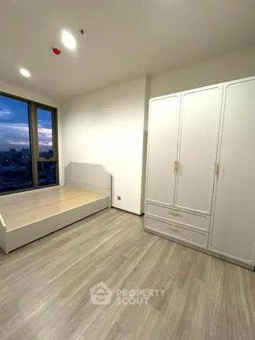 Spacious bedroom with large window offering stunning city views, featuring modern wardrobe and sleek flooring.