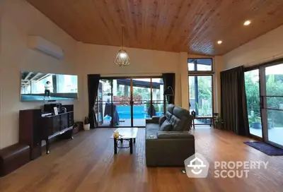 Spacious living room with high wooden ceilings, elegant hardwood floors, and large windows leading to a refreshing pool view, perfect for luxurious living.