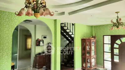 Charming living room with unique green wallpaper and elegant lighting fixtures, featuring a spiral staircase and wooden cabinet.