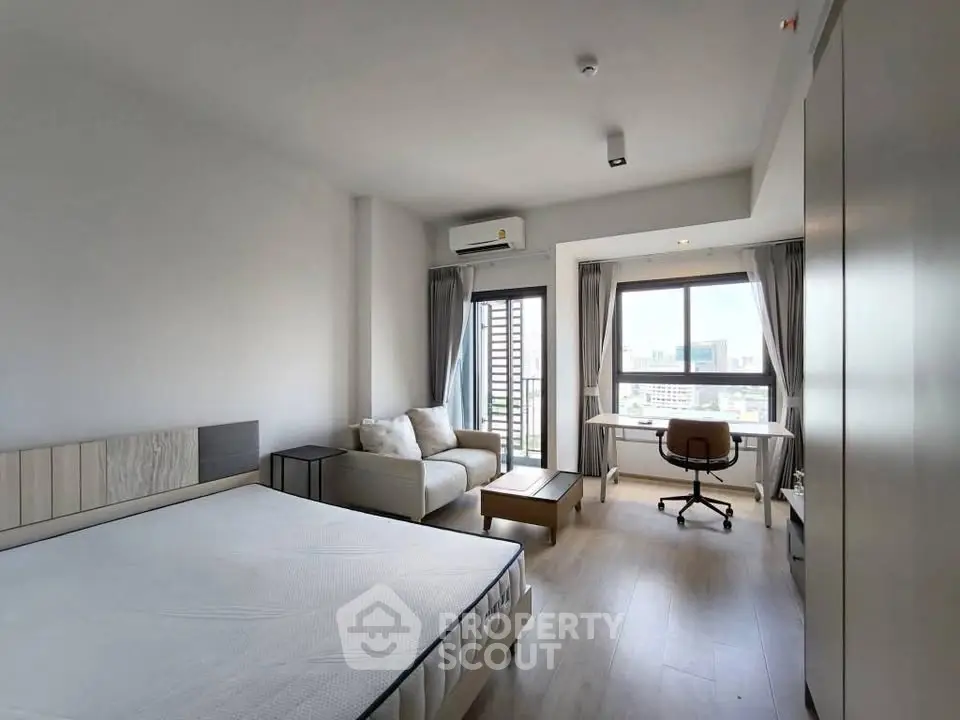 Spacious modern bedroom with city view, featuring a cozy seating area and work desk.