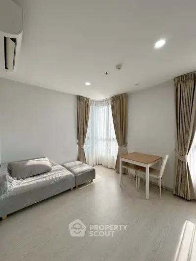 Bright and modern living room with cozy sofa and dining area, featuring large windows and elegant curtains.