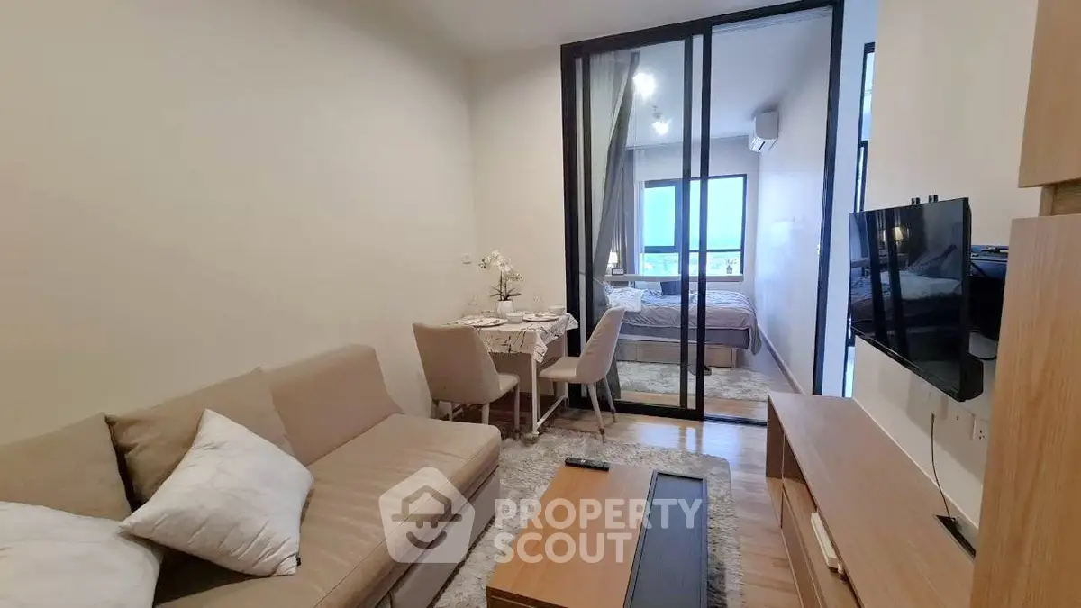 Modern living room with cozy sofa, dining area, and bedroom view in open-plan apartment.