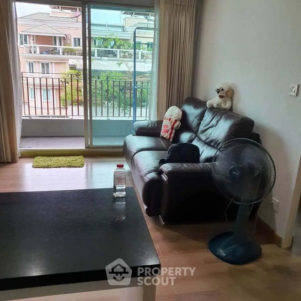Cozy living room with balcony view, featuring leather sofa and fan, perfect for relaxation.