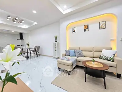 Modern living room with elegant decor and open dining area, featuring stylish lighting and cozy seating.