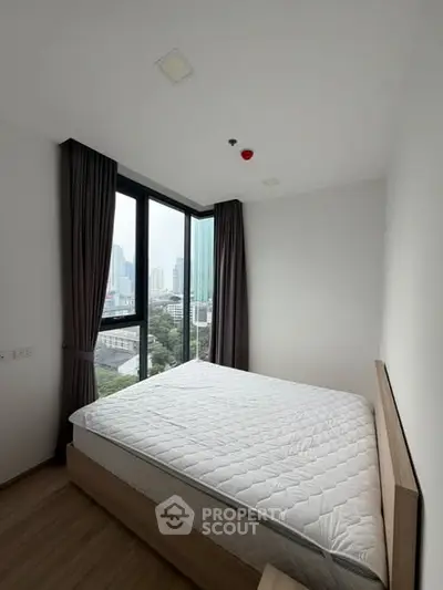 Modern bedroom with large windows offering city views in a high-rise apartment.