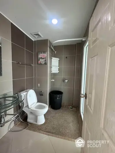 Modern bathroom with glass sink, toilet, and shower area in stylish brown tiles.