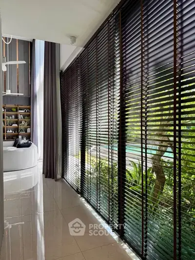 Luxurious living room with floor-to-ceiling windows and garden view, featuring elegant blinds and modern decor.