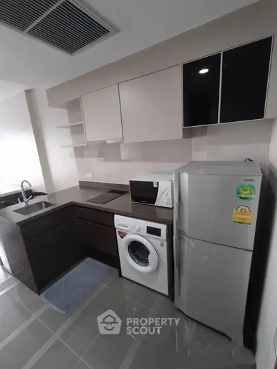 Modern kitchen with sleek cabinets, washing machine, and stainless steel fridge in compact layout.
