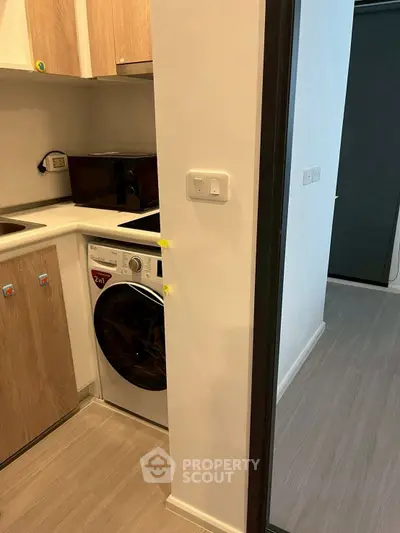 Compact kitchen with washing machine and microwave in modern apartment.