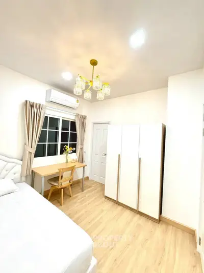 Bright and modern bedroom with elegant chandelier and cozy workspace.