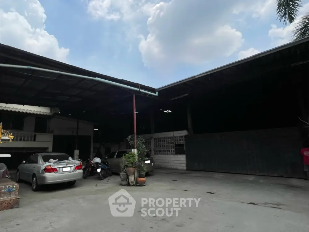 Spacious covered parking area with cars and motorcycles under a clear sky.