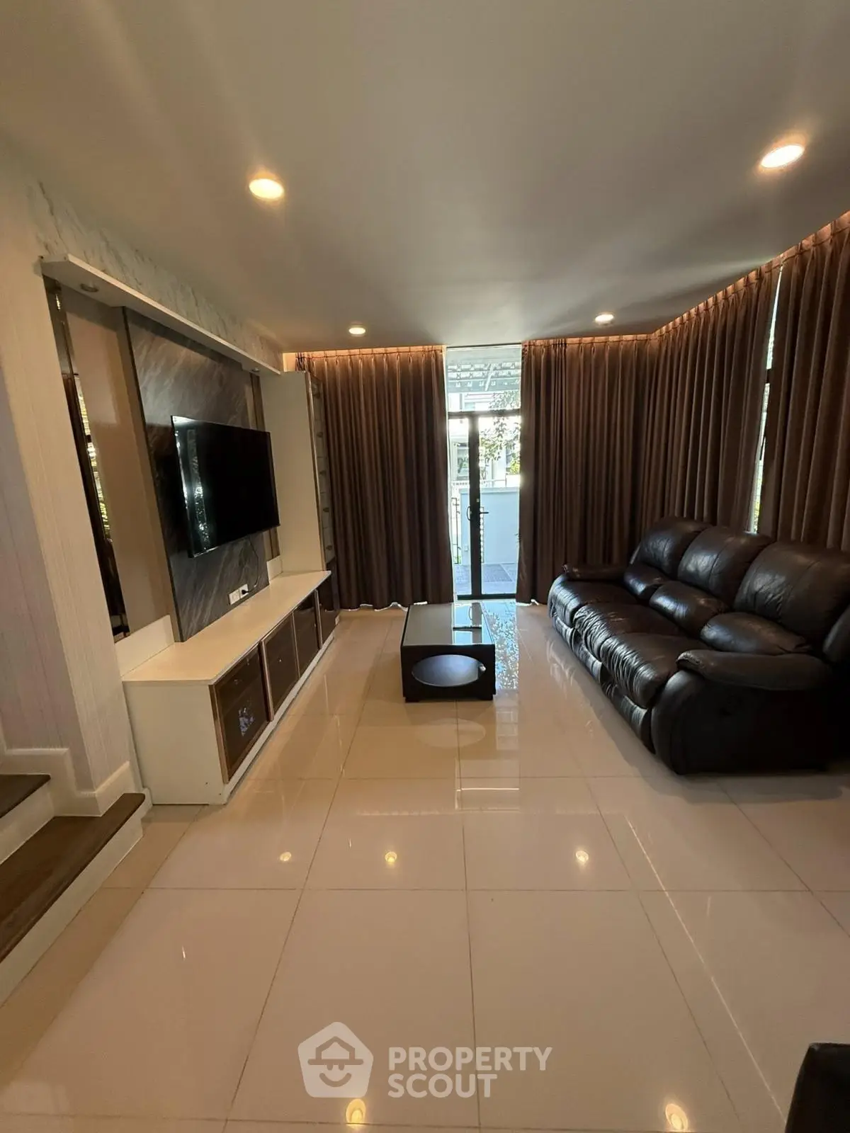 Modern living room with sleek leather sofa and wall-mounted TV, featuring elegant curtains and glossy tile flooring.