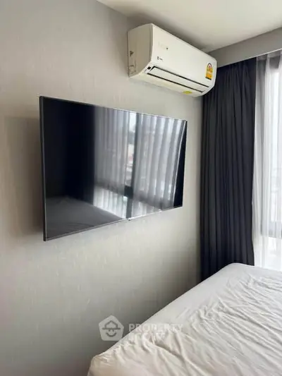 Modern bedroom with wall-mounted TV and air conditioning unit, featuring sleek design and natural light.