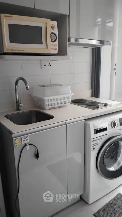 Compact kitchen with modern appliances including washing machine and microwave, ideal for urban living.