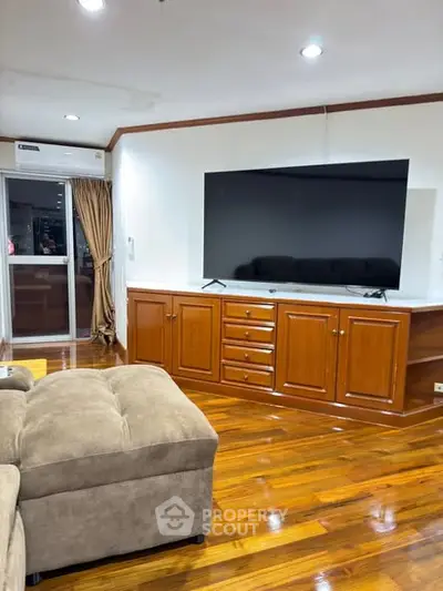 Spacious living room with polished wooden floors and large flat-screen TV, perfect for entertainment.