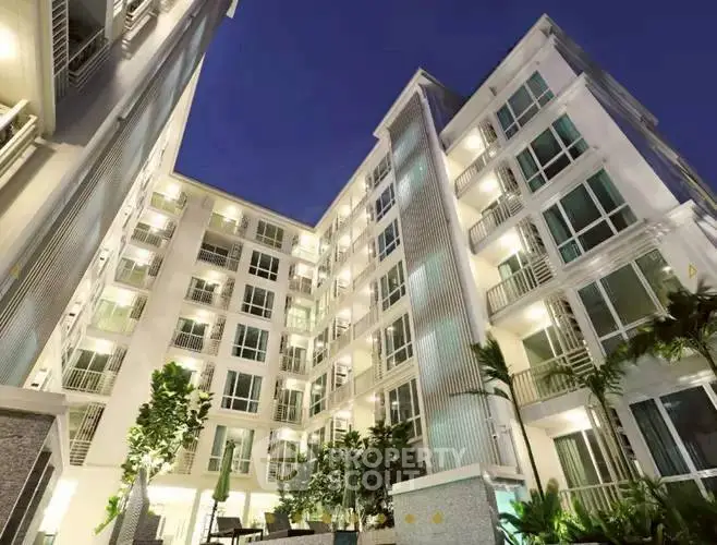 Modern apartment building with illuminated facade and lush greenery at dusk.