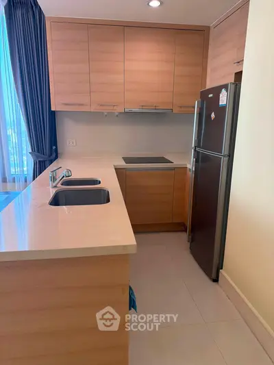 Modern kitchen with sleek wooden cabinets and stainless steel fridge in a cozy apartment.