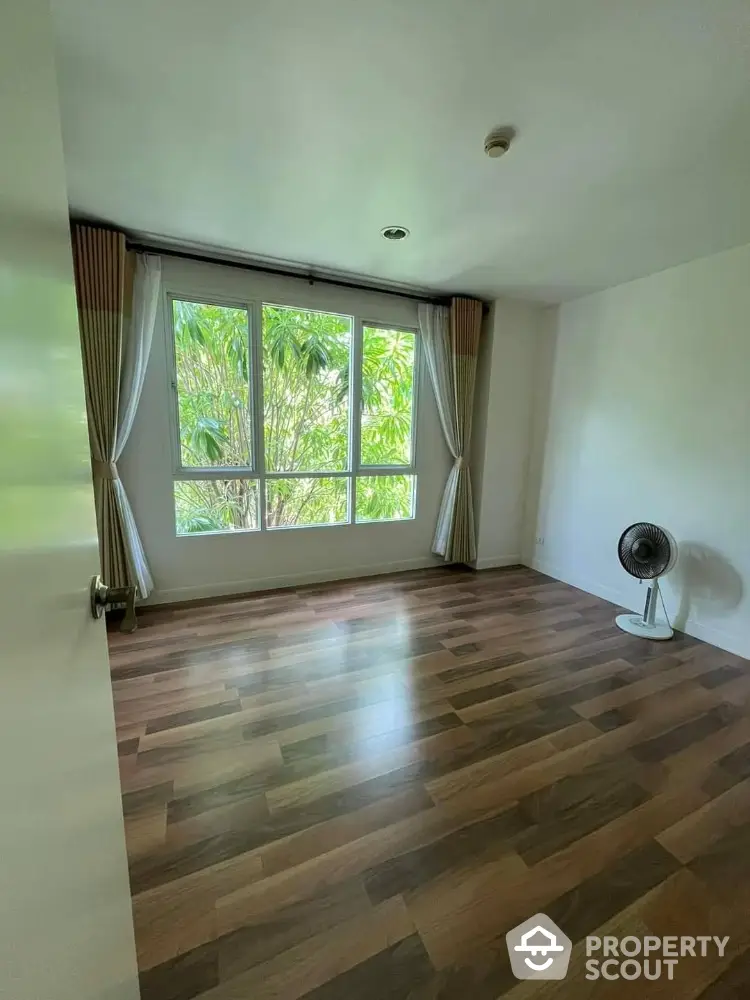 Spacious empty room with large window and wooden flooring, ideal for customization.