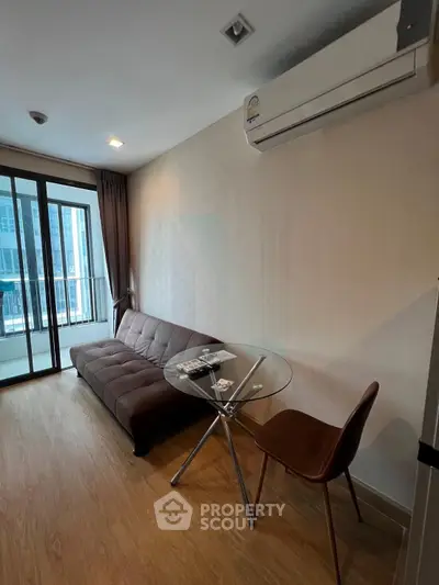 Modern living room with sleek sofa and glass table, featuring large windows and air conditioning.