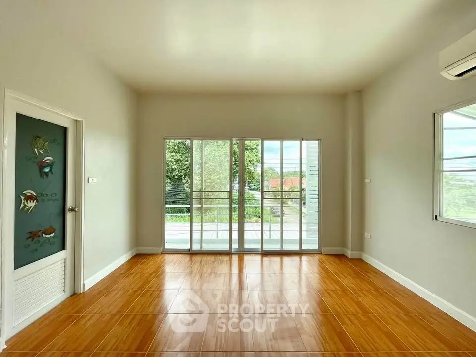 Spacious room with wooden flooring and large windows opening to a balcony with a view.