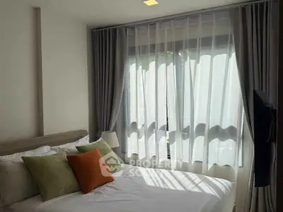 Cozy bedroom with large window and stylish curtains, featuring a comfortable bed with decorative pillows.