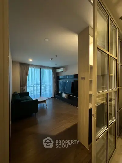 Modern living room with wooden flooring and large window, featuring a sleek entertainment unit and cozy sofa.