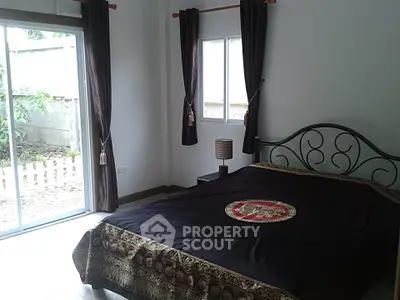 Cozy bedroom with elegant bedspread and garden view through sliding glass door.