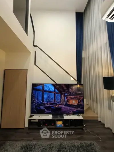 Modern living room with high ceilings and stylish staircase, featuring a large TV and elegant decor.
