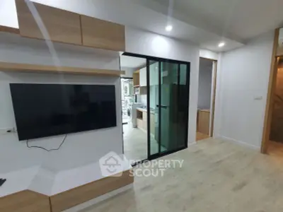 Modern living area with sleek TV setup and glass sliding doors leading to kitchen.