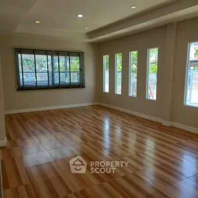 Spacious empty living room with large windows and wooden flooring, perfect for customization.