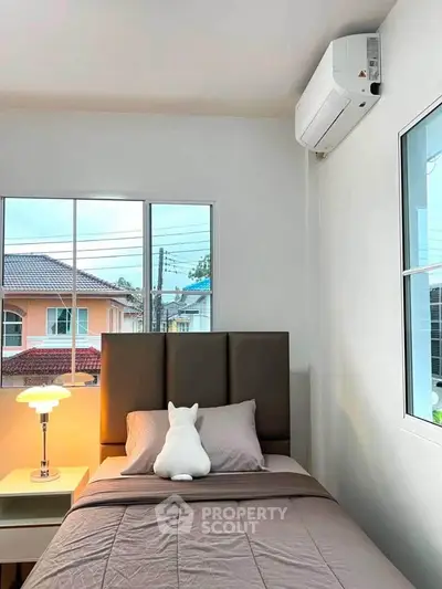 Cozy bedroom with modern decor and large window offering natural light and neighborhood view.