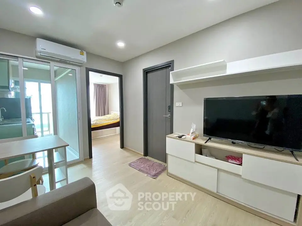 Modern apartment living room with TV and dining area, open view to bedroom and kitchen.