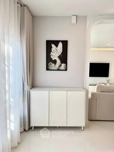 Elegant living room with modern decor and stylish artwork, featuring a sleek white cabinet and soft natural lighting.
