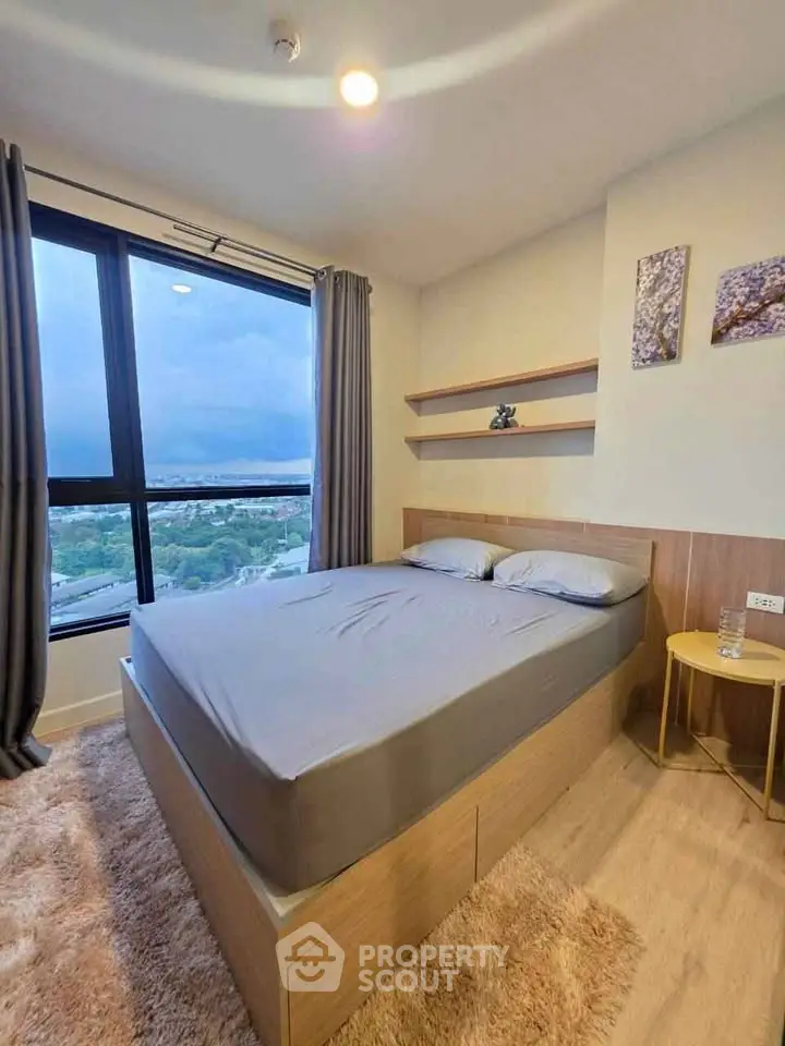 Modern bedroom with large window offering stunning city view, cozy decor, and elegant furnishings.