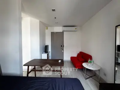 Modern studio apartment with minimalist decor, featuring a red sofa and wooden table, ideal for urban living.