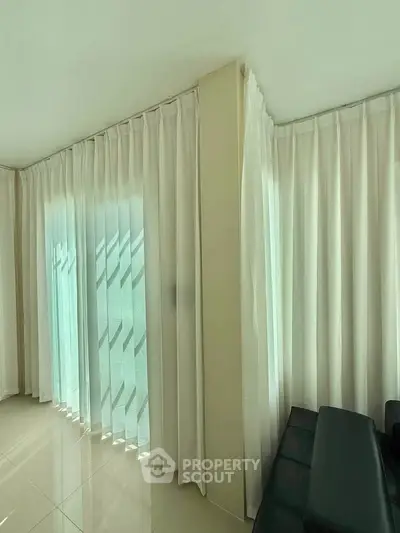 Spacious corner living room with elegant floor-to-ceiling curtains and glossy tiled flooring.