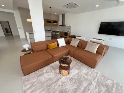 Spacious modern living room with stylish brown leather sectional and open kitchen layout.