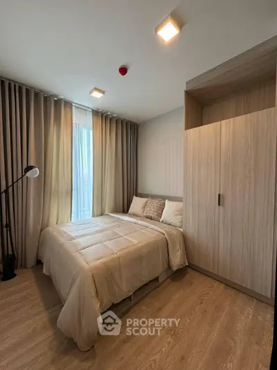 Cozy modern bedroom with wooden flooring and large window, featuring a stylish wardrobe and elegant lighting.