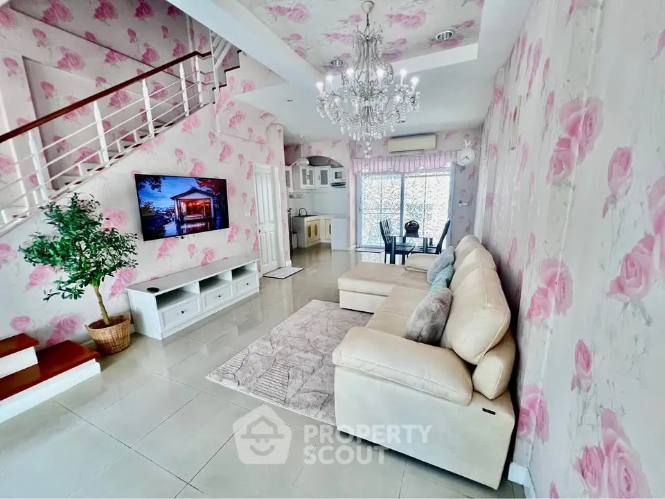 Charming living room with floral wallpaper, elegant chandelier, and cozy seating area.