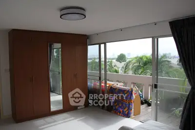 Spacious bedroom with balcony and city view, featuring large wardrobe and natural light.