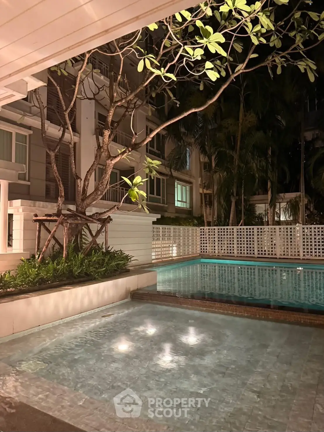 Luxurious residential pool area with ambient lighting and lush greenery at night.