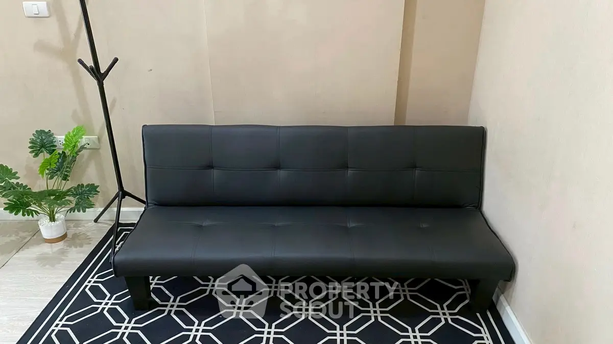 Modern black leather sofa in stylish living room with geometric rug and plant decor.