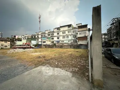 Vacant land plot with urban residential buildings in the background, ideal for development.