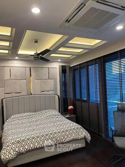 Luxurious bedroom with modern ceiling design and large windows with blinds.