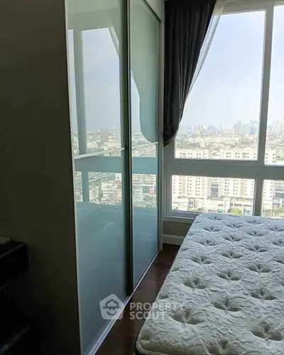 Modern bedroom with city view and large window, featuring a comfortable mattress and sleek wardrobe.