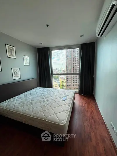 Spacious bedroom with large window offering stunning city views, featuring elegant wood flooring and modern decor.
