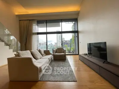 Spacious modern living room with large windows and city view, featuring elegant furniture and wooden flooring.