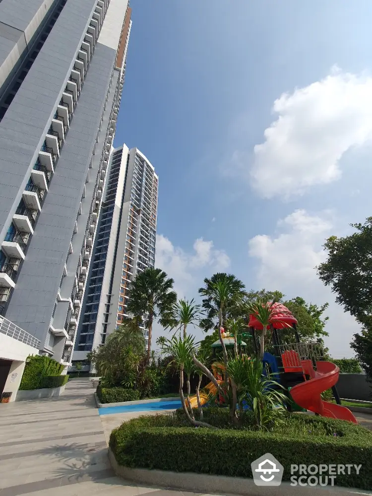 Stunning high-rise building with lush garden and vibrant playground under a clear blue sky.