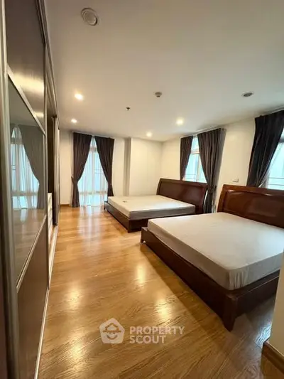 Spacious bedroom with two beds and wooden flooring, featuring large windows and elegant curtains.